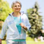 Frau geht zügig durch einen sommerlichen Park beim Intervall-Walking