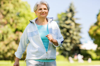 Frau geht zügig durch einen sommerlichen Park beim Intervall-Walking